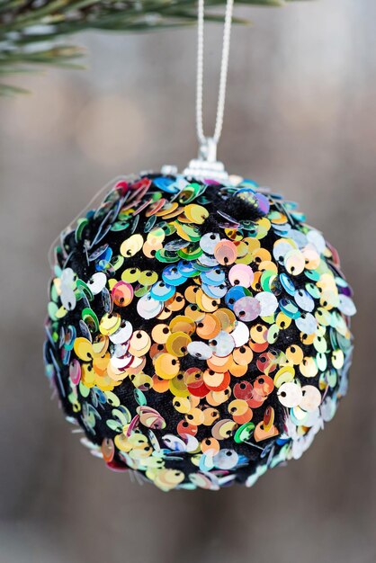 Photo hanging multi colored glitter christmas ball on spruce and over blurred background