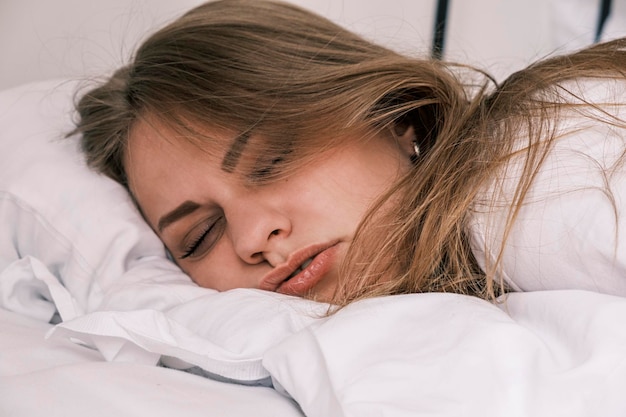 Hangover closeup the grimacing face of a sleeping young woman the morning after drinking alcohol the