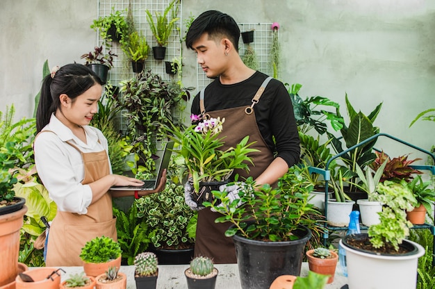 Happily Asian young gardener couple wearing apron use garden equipment and laptop computer to take care