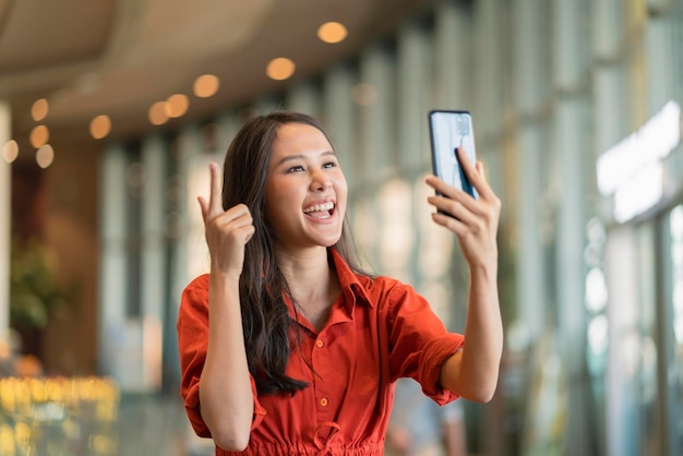 Happiness asian female woman smile hand wave give a kiss to family via video call smartphone device social distancing greeting with blur mall background new normal lifestyle