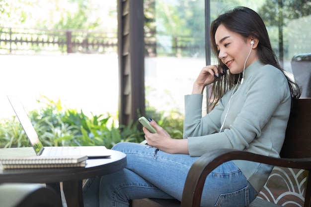 Happiness Asian woman listening music and using laptop at coffee shop Relaxing time