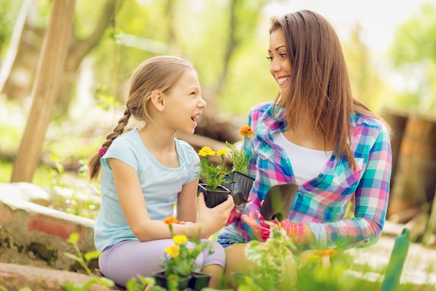 Happiness cute little girl and smiling young woman planting flowers in a backyard.