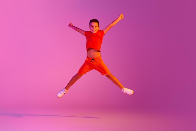 Happiness emotional kid in casual bright clothes jumping isolated over pink background in neon