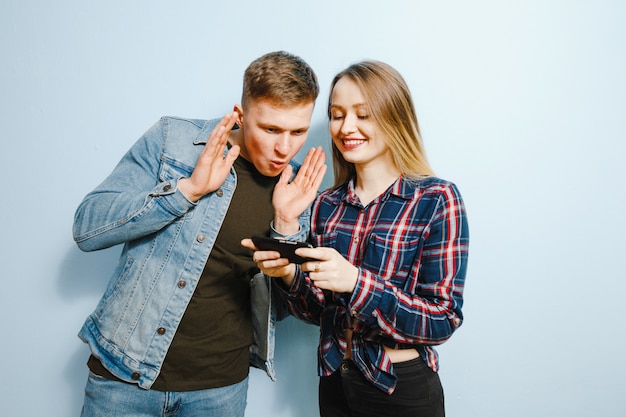 Happiness on the face of two friends, over blue background, looking at the phone.