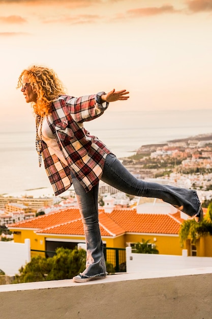 Happiness and freedom concept for independent young beautiful woman walking balanced on a wall with city and sea coast in background summer holiday vacation and travel free lifestyle