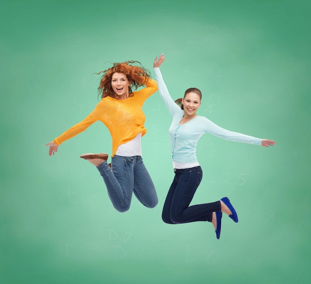 happiness, freedom, friendship, education and people concept - smiling young women jumping in air over green board background