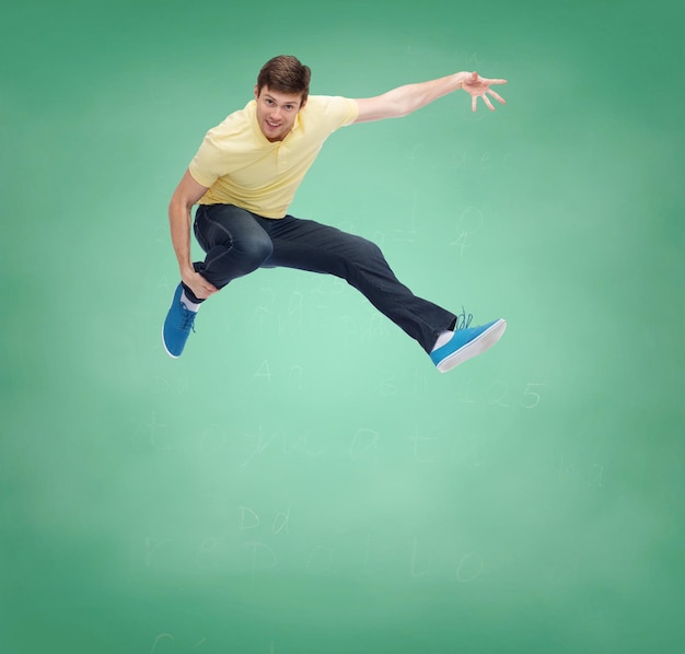 happiness, freedom, movement, education and people concept - smiling young man jumping in air over over green board background