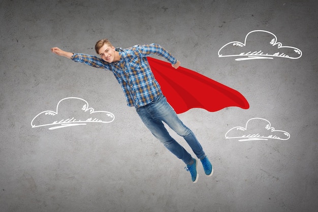 happiness, freedom, movement and people concept - smiling young man flying in air over blue background concrete wall with drawing of clouds background