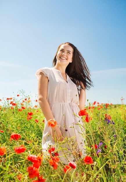 happiness, nature, summer, vacation and people concept - smiling young woman on poppy field