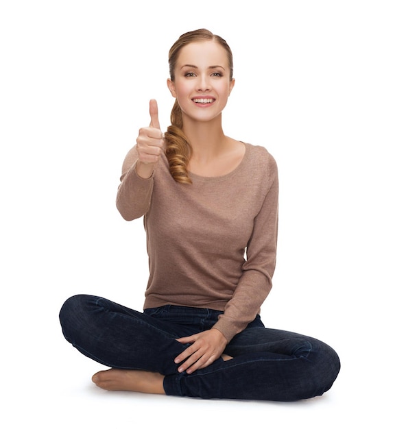 happiness and people concept - smiling young woman sitting on floor and showing thumbs up