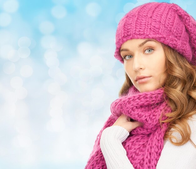 happiness, winter holidays, christmas and people concept - young woman in pink hat and scarf over blue lights background