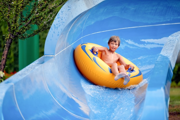 Happy an 8 year old boy is riding in the water Park on inflatable circles on water slides with splash