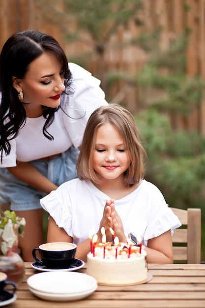 Happy adorable girl with mom celebrate with birthday cake in cafe terrace. 10 year old celebrate birthday.