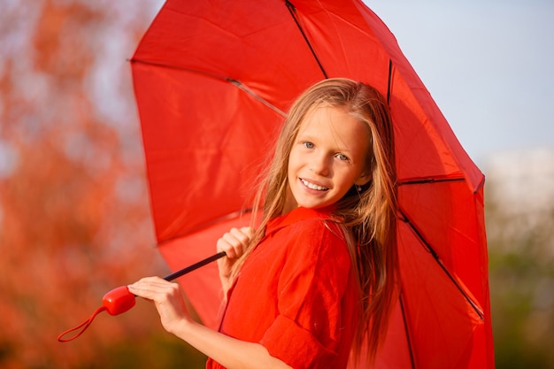 Happy adorable girl with red umbrella at autumn