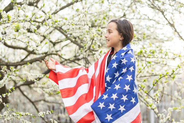 Happy adorable little girl smiling and waving American flag. Patriotic holiday. Happy kid, cute little child girl with American flag. USA celebrate 4th of July. Independence Day concept.