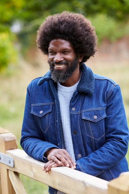 Happy adult black man leaning on a wooden fance in the countryside smiling close up