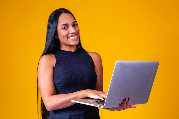 Happy adult business lady in elegant dress looking at camera while working on laptop against yellow background