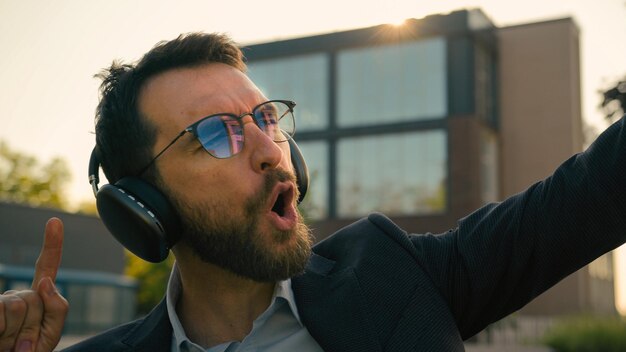 Photo happy adult caucasian man cheerful joyful businessman in headphones dancing in city outdoors winning