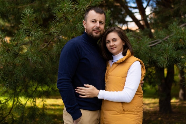 Happy adult husband and wife in the autumn forest stand embracing