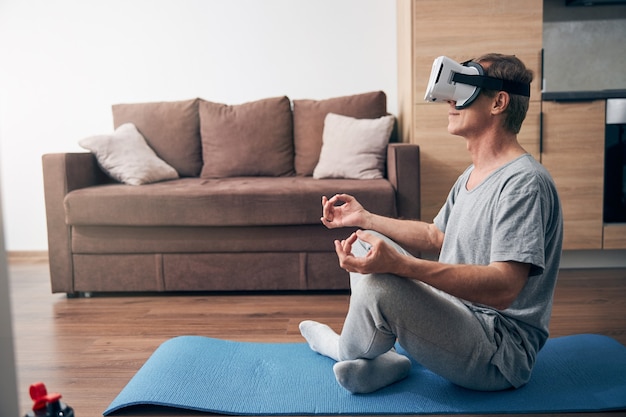 Happy adult male person keeping smile on his face while enjoying virtual yoga practice in room