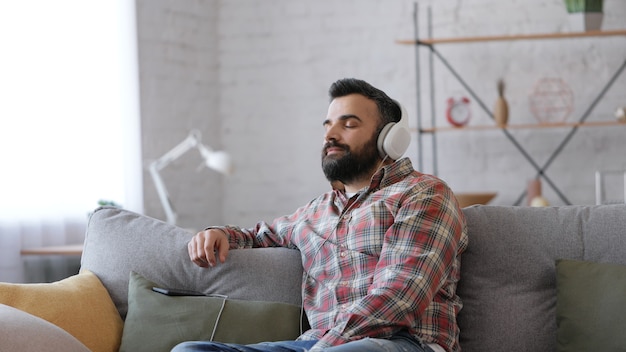 Happy adult man in white headphones enjoy listening favorite music on smartphone using music app.