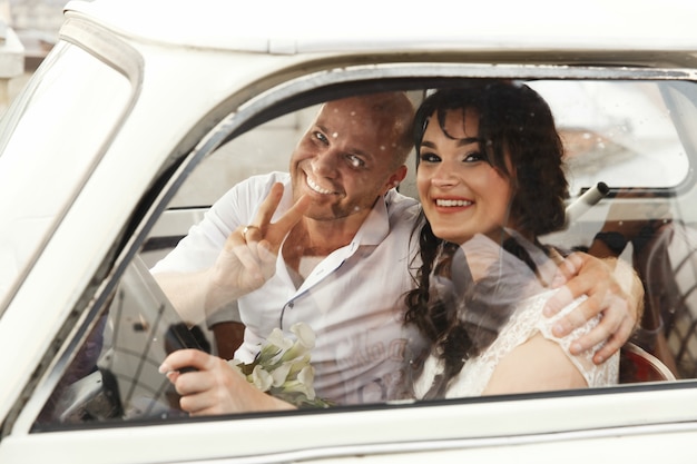 Happy adult wedding couple sits in the old car on the roof 