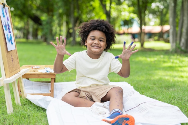 Happy African American boy showing hands after painting watercolor on white paper in park