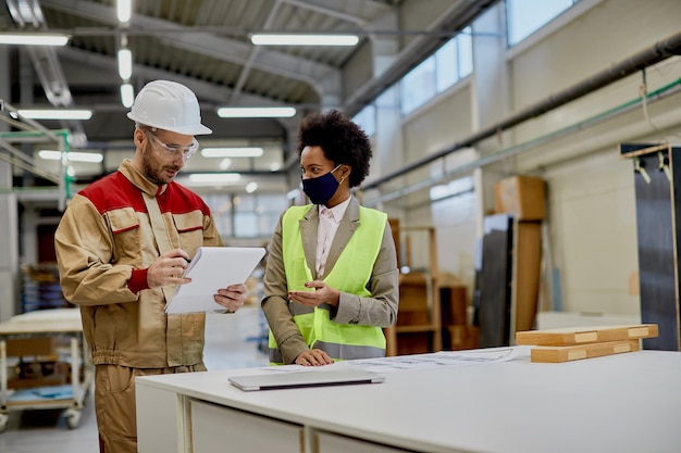 Happy African American businesswoman talking to a worker at woodworking factory