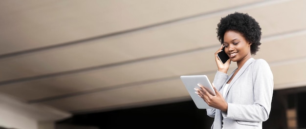 Happy african american businesswoman with smartphone and tablet outdoors free place