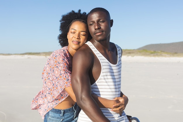 Happy african american couple embracing and smiling with eyes closed on sunny beach. Summer, romance, freedom, relaxation, togetherness and vacation, unaltered.