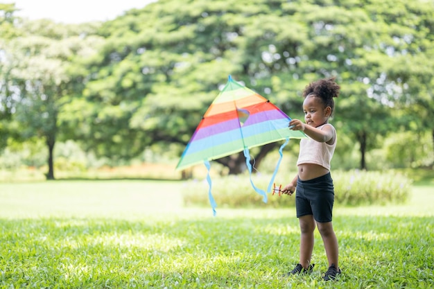 Happy African American cute little girl enjoys playing with kite in park on holidays in summer