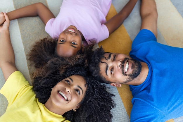 Happy african american family of four bonding lying on bed black parents and cute little daughter with smiling faces looking at camera in bedroom mixed race mom dad with child portrait top view