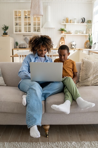 Happy african american family mother and little kid son watching cartoons on laptop together