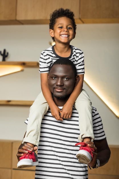 Happy african american father carrying cute little son on neck and smiling at camera