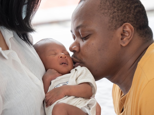 Happy African American father kisses two weeks newborn baby son in mother's embrace holding baby