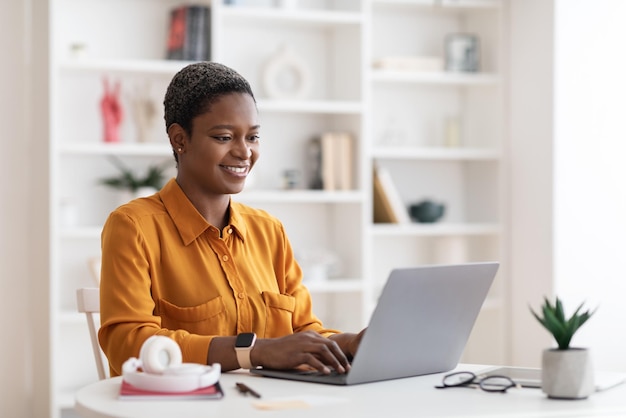 Happy african american lady freelancer using laptop at home