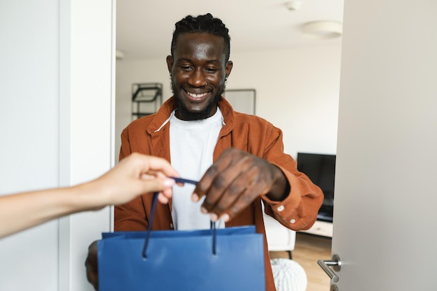 Happy african american male customer receiving colorful shopping bag woman delivering his order