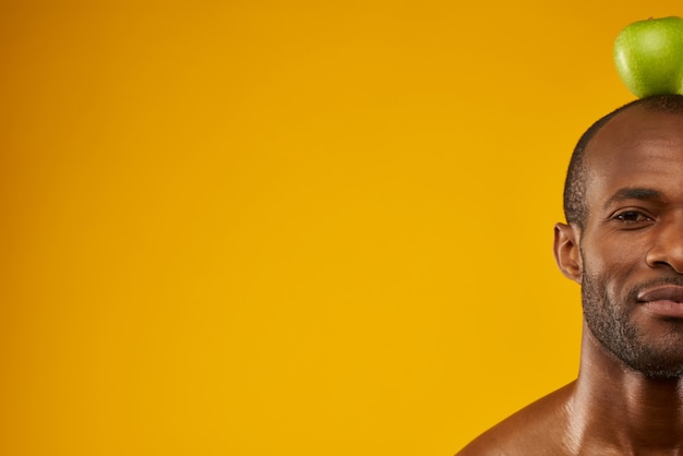 Happy African American man holds apple on top of head.