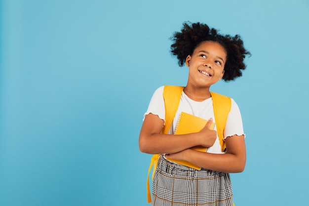 Happy African American schoolgirl holding books on blue background back to school concept