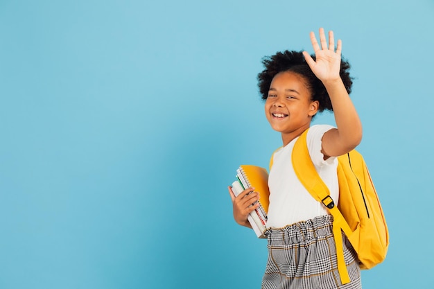 Happy African American schoolgirl makes a welcome hand gesture on blue background back to school concept