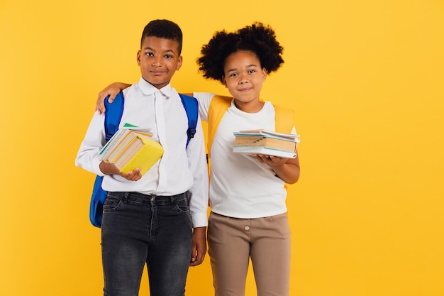 Happy african american schoolgirl and mixed race schoolboy holding books on yellow background copy space