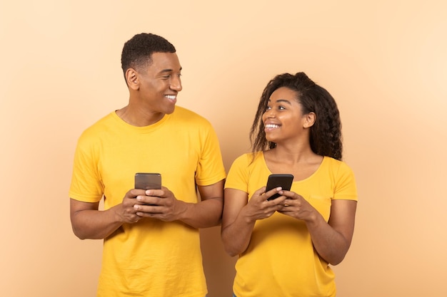 Happy african american spouses using cellphones networking or chatting with friends looking at each other