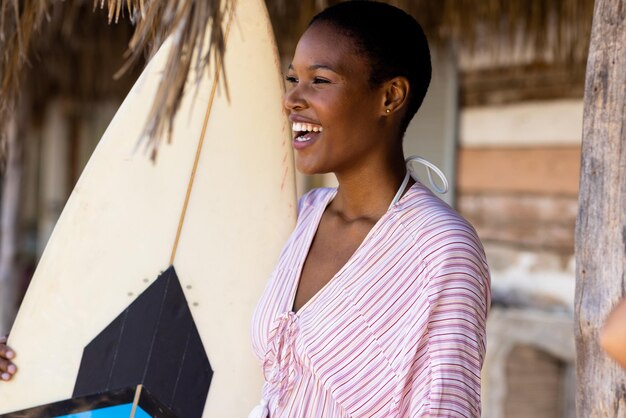 Happy african american woman holding surfboard at beach. Spending quality time, lifestyle, summertime and vacation concept.