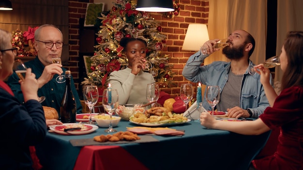 Happy african american woman inviting family members to toast while celebrating winter holiday at home. Festive multiethnic relatives gathered in dining room to celebrate Christmas.