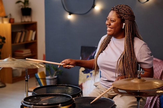 Happy african american woman playing drums during repetition in musical studio