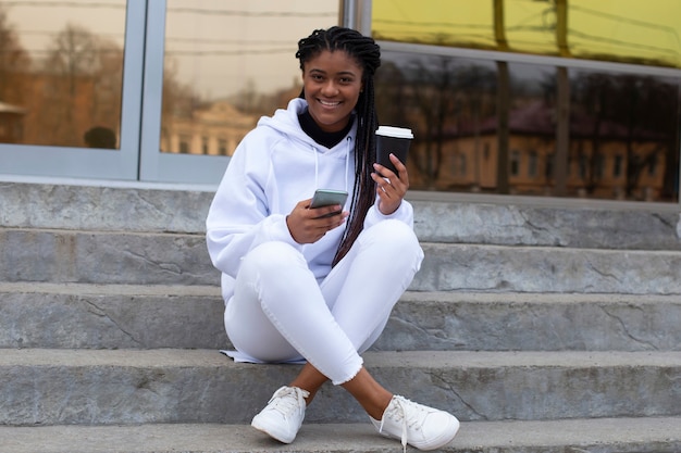 The happy african american woman on the street with phone and coffee