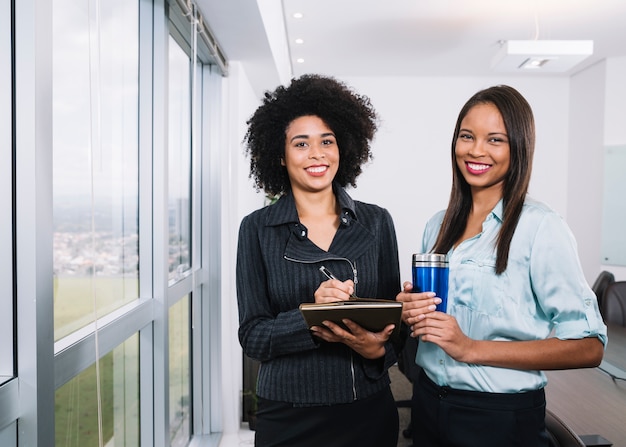 Happy African American women with documents and thermos near window in office