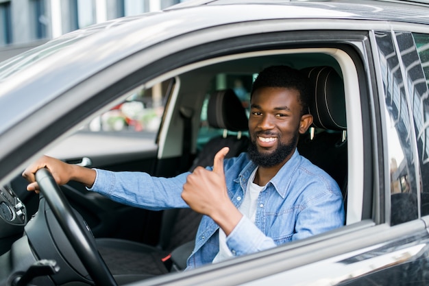 Happy african businessman giving thumb up inside new car