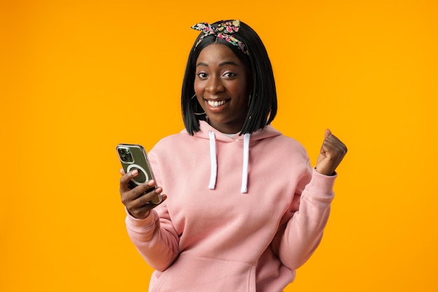 Happy african girl using her smartphone against yellow background