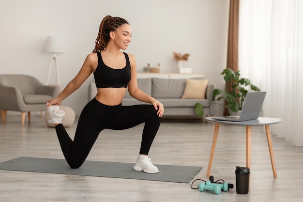 Happy african lady doing hip and leg exercises at home